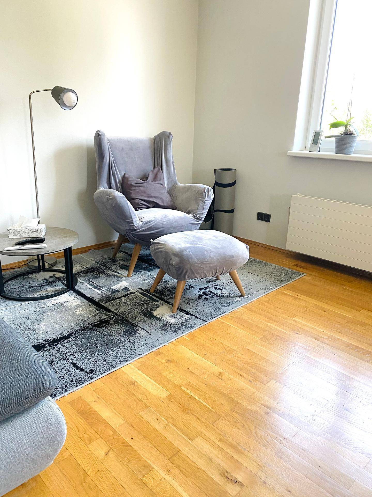 Gemütliches Wohnzimmer mit Sessel, Stehlampe und Holzboden in hellem Ambiente.