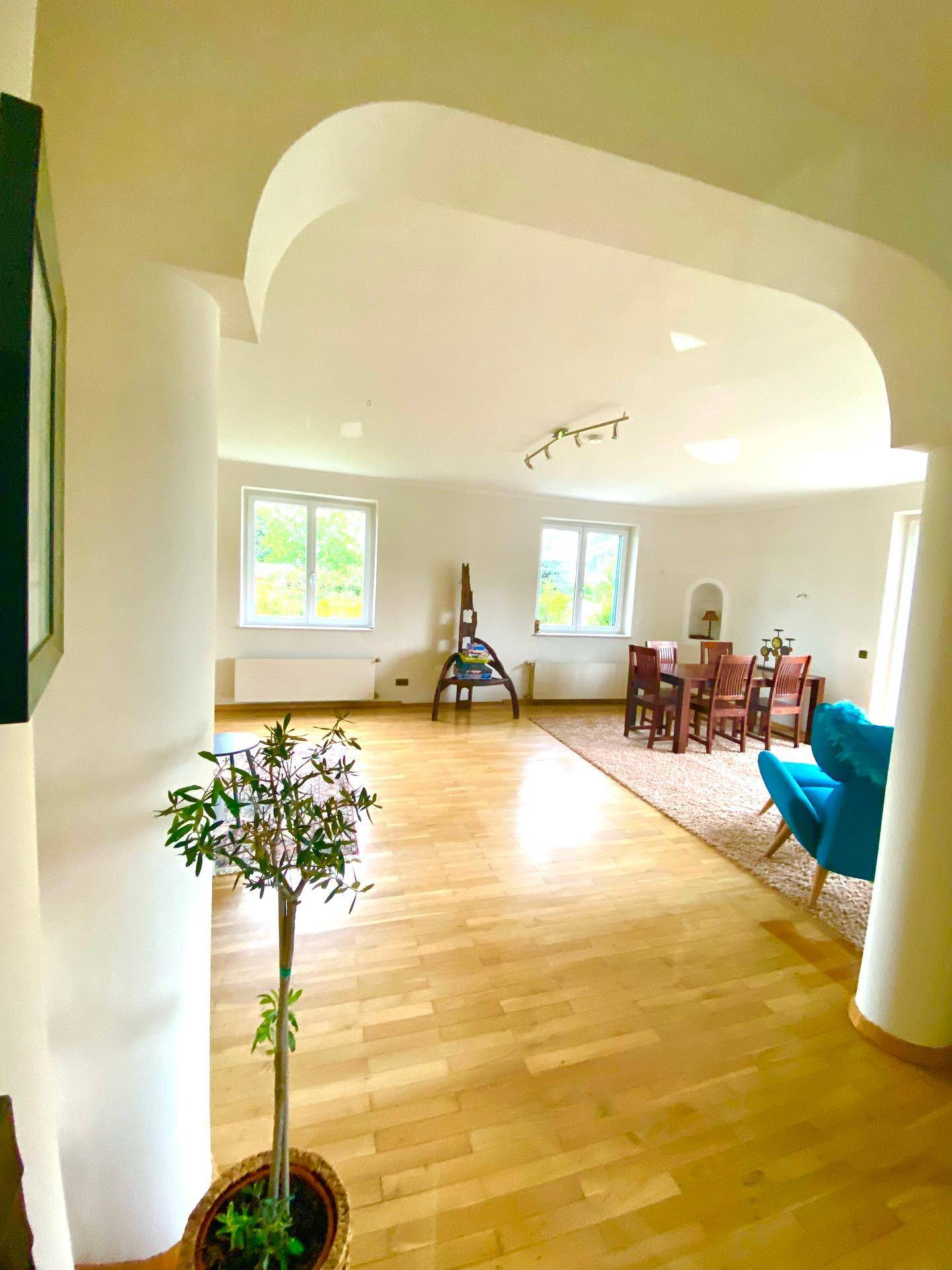 Heller Wohn- und Essbereich mit Holzboden, großen Fenstern und eleganten Bögen.
