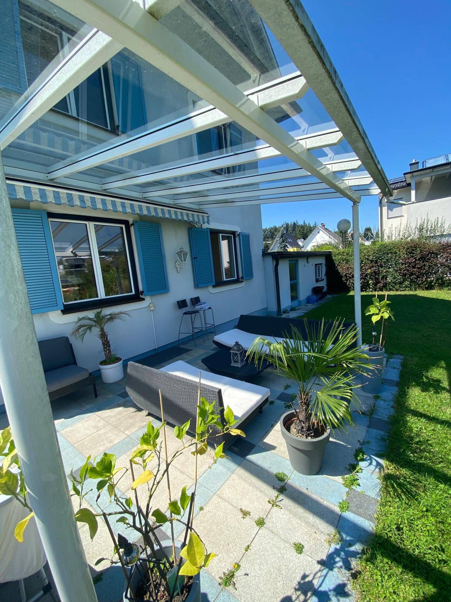 Überdachte Terrasse mit modernen Gartenmöbeln und Zugang zum gepflegten Rasenbereich.