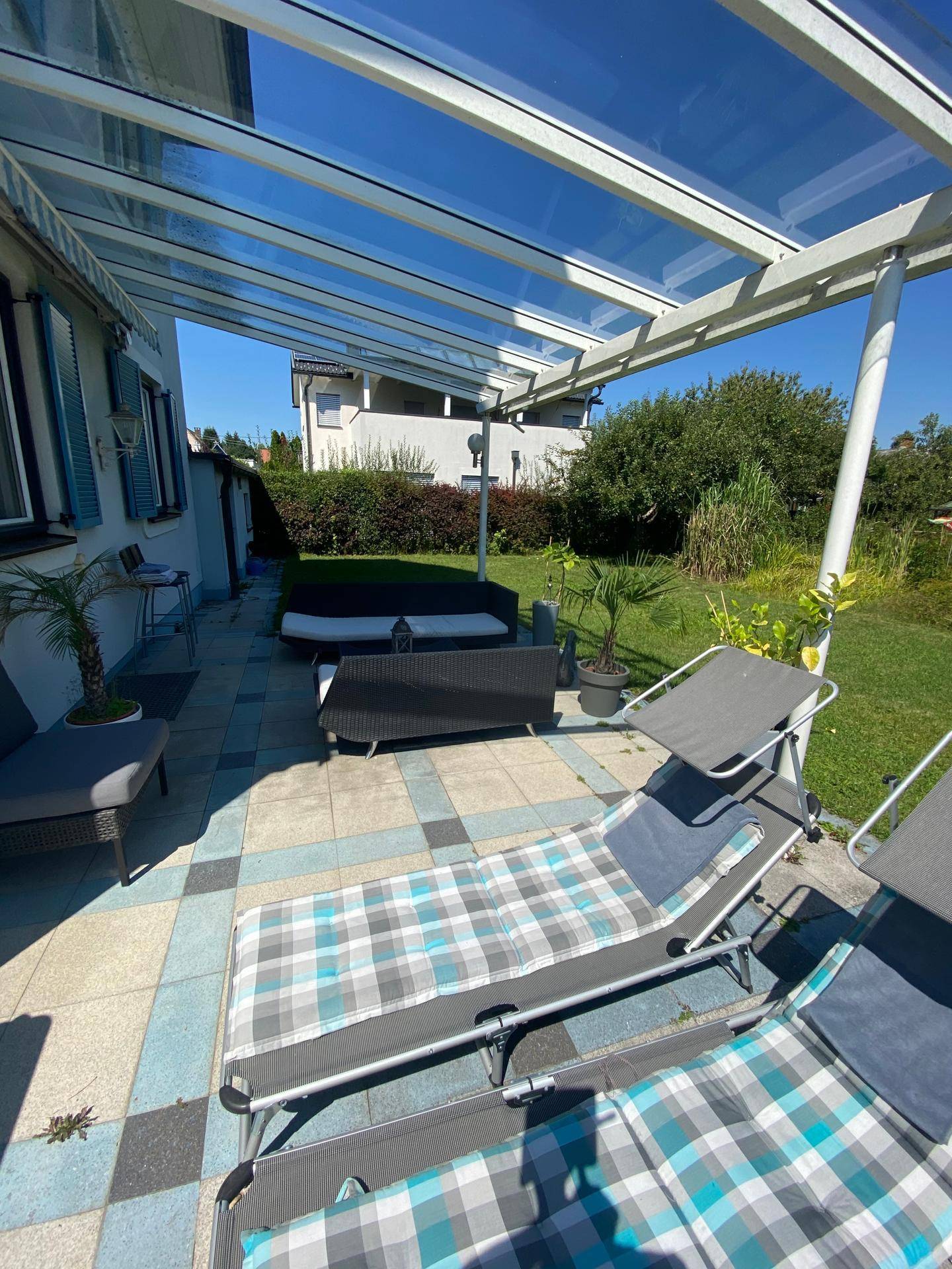 Überdachte Terrasse mit Sonnenliegen und Blick auf den weitläufigen Gartenbereich.