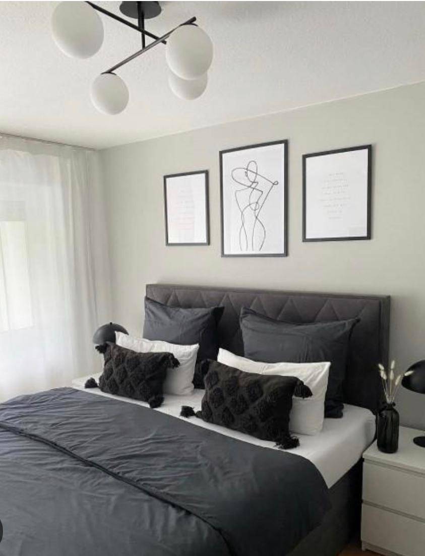 Modern eingerichtetes Schlafzimmer mit dunklem Bett, minimalistischer Kunst und stilvoller Beleuchtung.