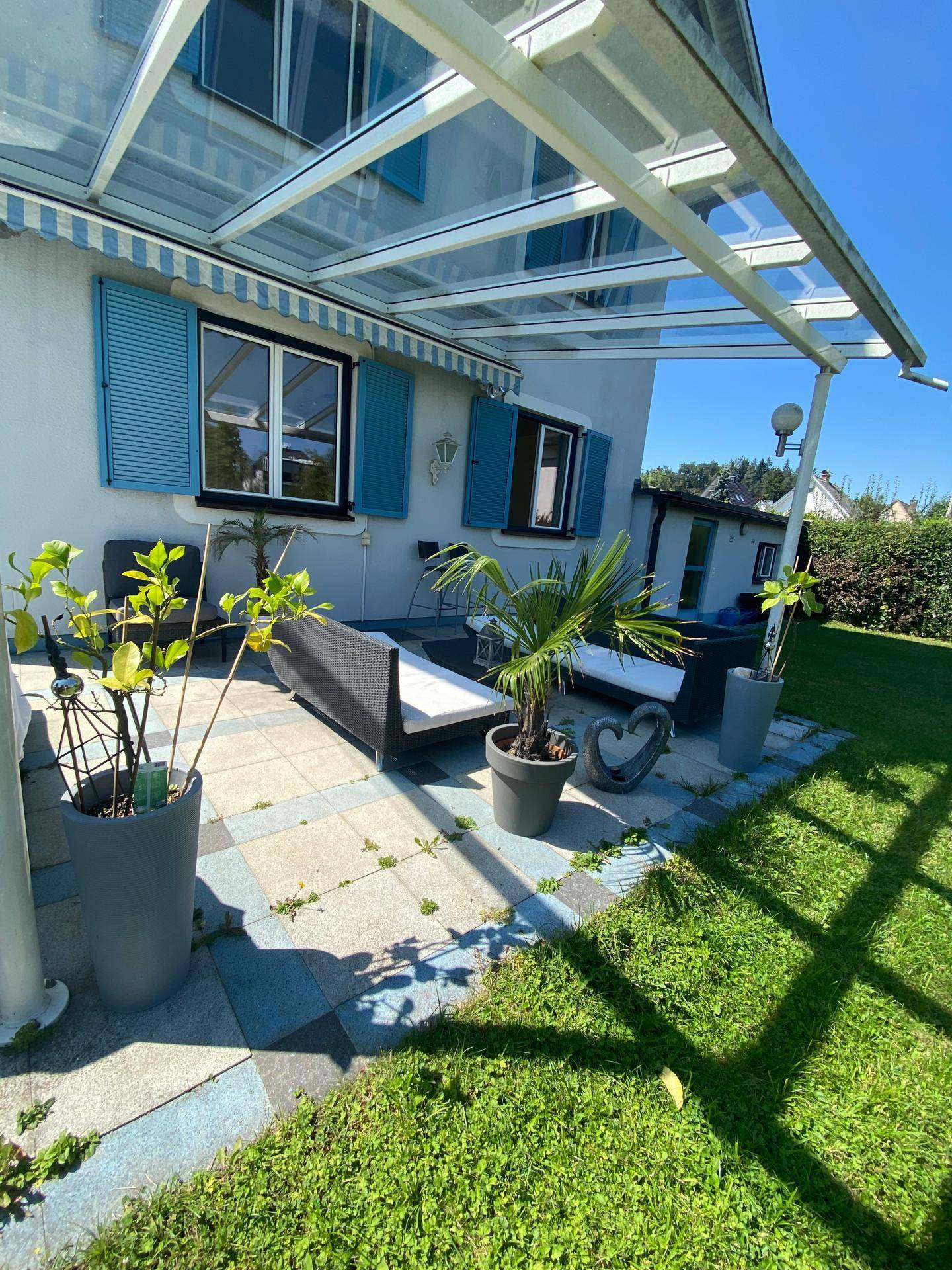 Helle Terrasse mit Glasüberdachung, Pflanzen und direktem Zugang zum Garten.