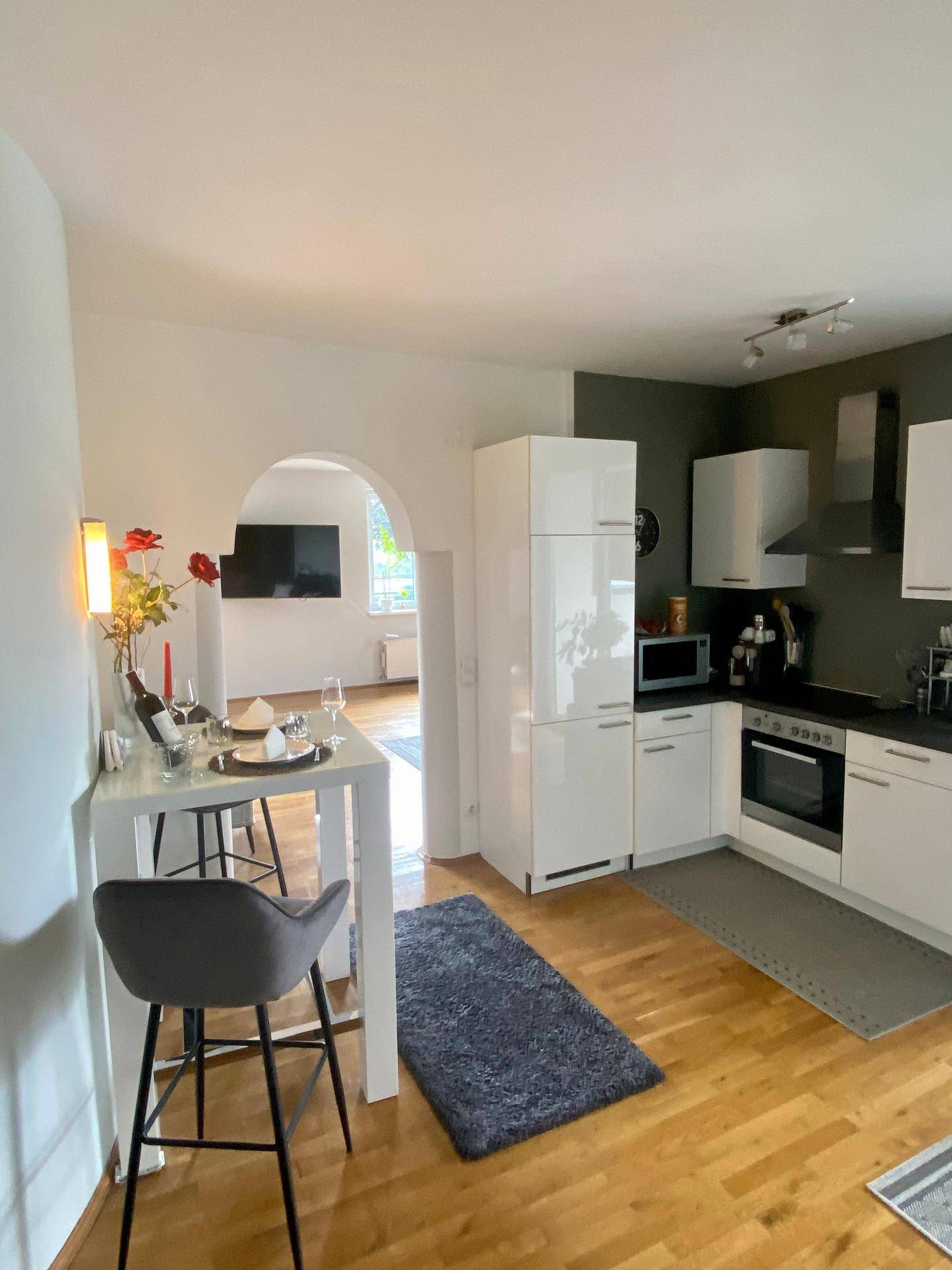 Moderne Küche mit Essbereich, weißen Hochglanzfronten und Holzboden.