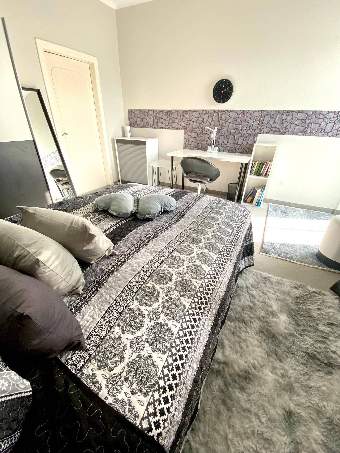Gemütliches Schlafzimmer mit Bett, Schreibtisch und einem großen Spiegel, der den Raum optisch erweitert.