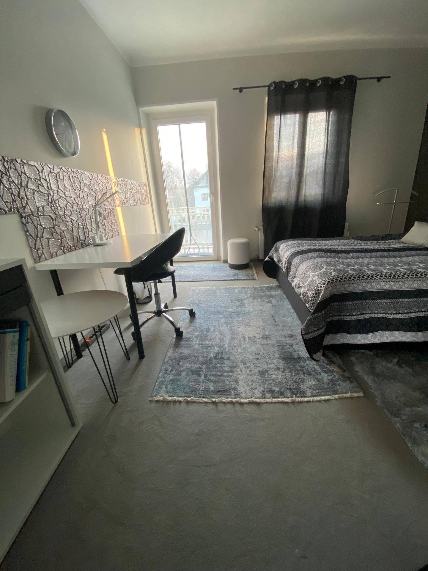 Schlafzimmer mit Schreibtischbereich, Teppichboden und Tür zum Außenbereich, gut beleuchtet.