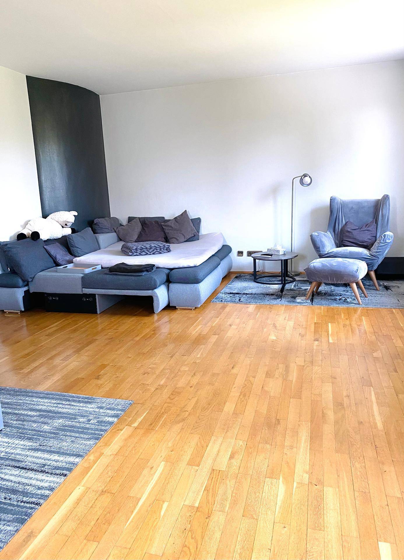 Geräumiges Wohnzimmer mit großem Ecksofa, Holzboden und einer modernen Akzentwand in dunklem Grau.