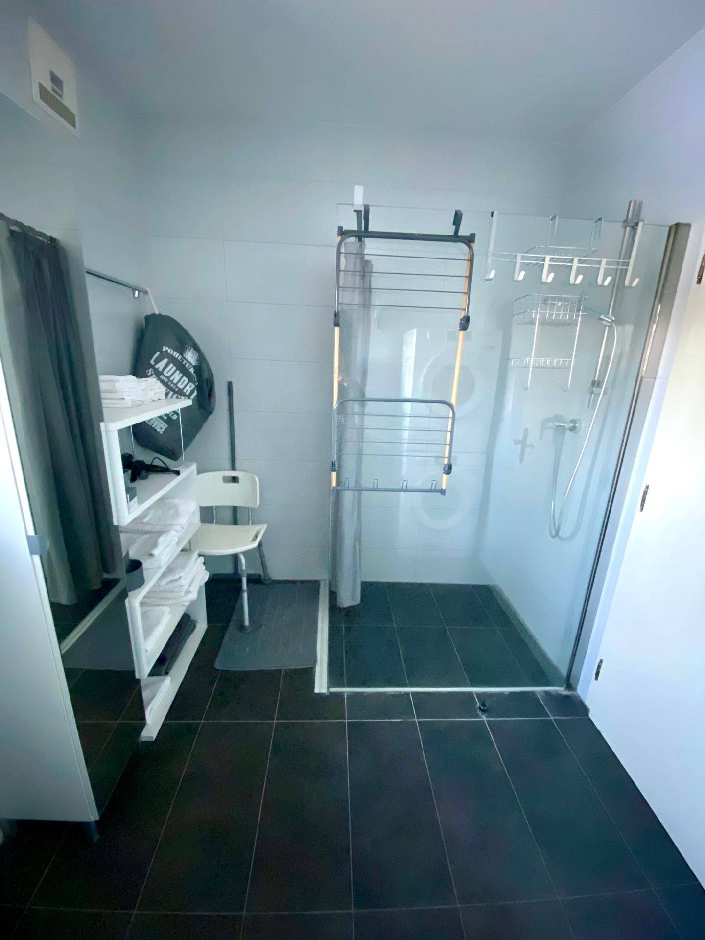 Modernes Badezimmer mit ebenerdiger Dusche, Ablagen und einem Wäschekorb, sehr funktional.