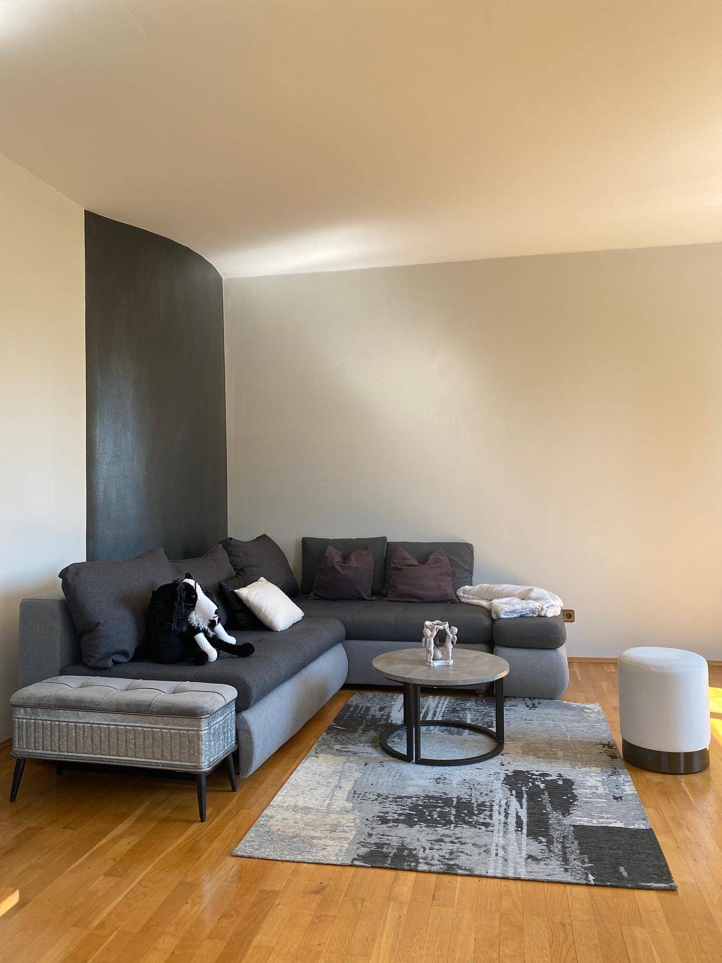 Gemütliches Wohnzimmer mit Ecksofa, Couchtisch und einem modernen Teppich auf dem Holzboden.