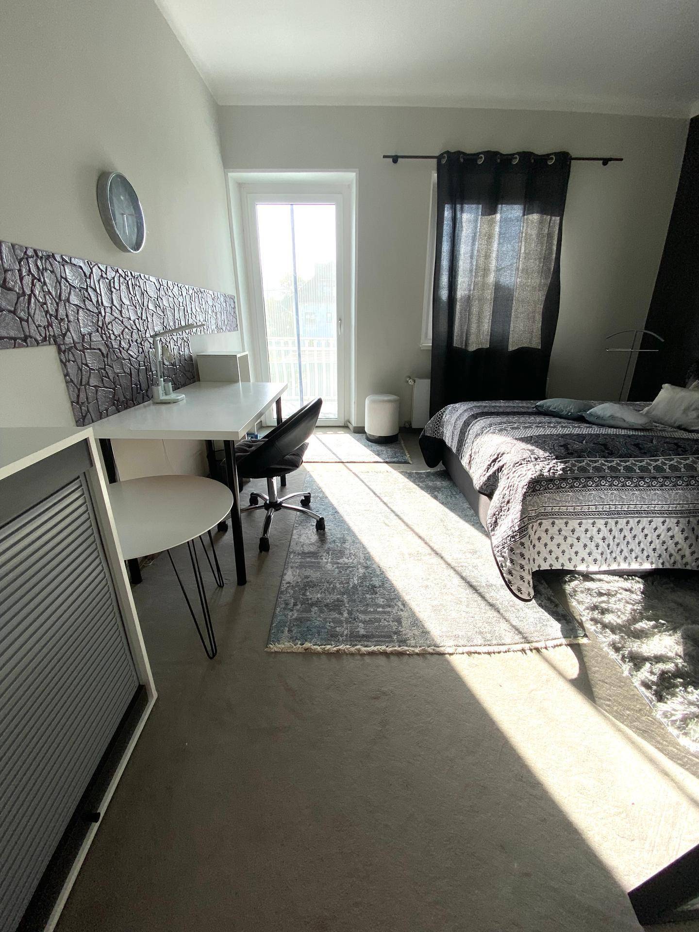 Schlafzimmer mit Schreibtisch, Bett und Zugang zu einem Balkon oder einer Terrasse.