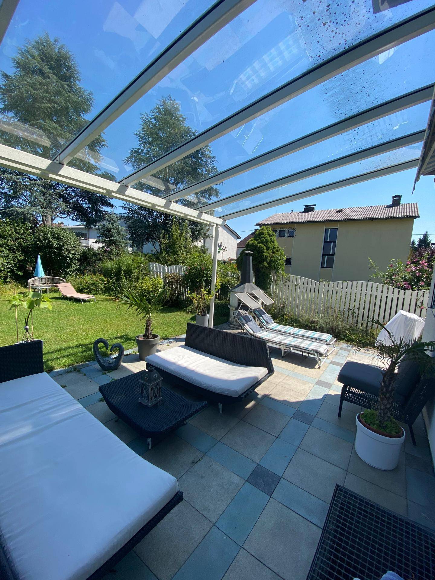 Geräumige überdachte Terrasse mit bequemen Liegen und Blick auf den grünen Garten.