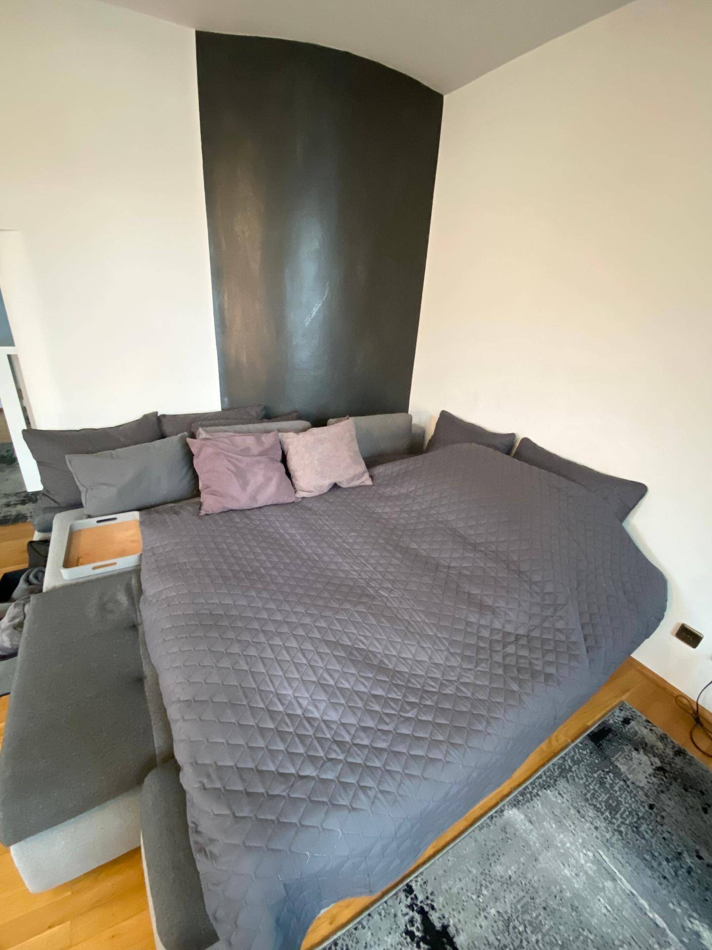 Großes Ecksofa, als Schlafgelegenheit hergerichtet, mit vielen Kissen und einer grauen Decke.