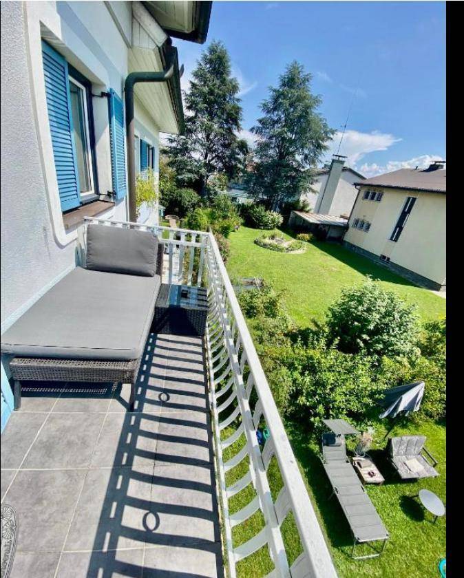Balkon mit Blick auf einen gepflegten Garten und Liegestühlen, sonnig und grün.