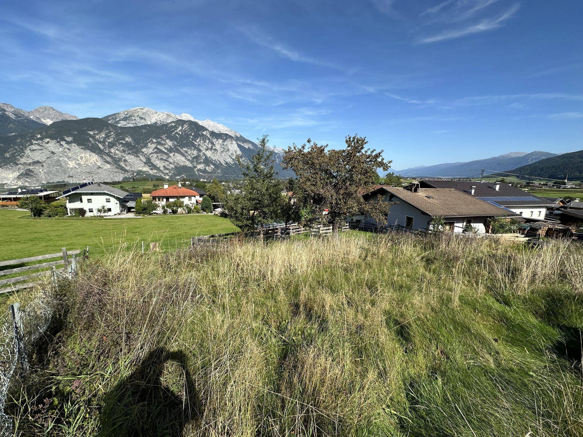 Idyllische Landschaft mit grünen Wiesen, vereinzelten Häusern und einer beeindruckenden Bergkulisse.