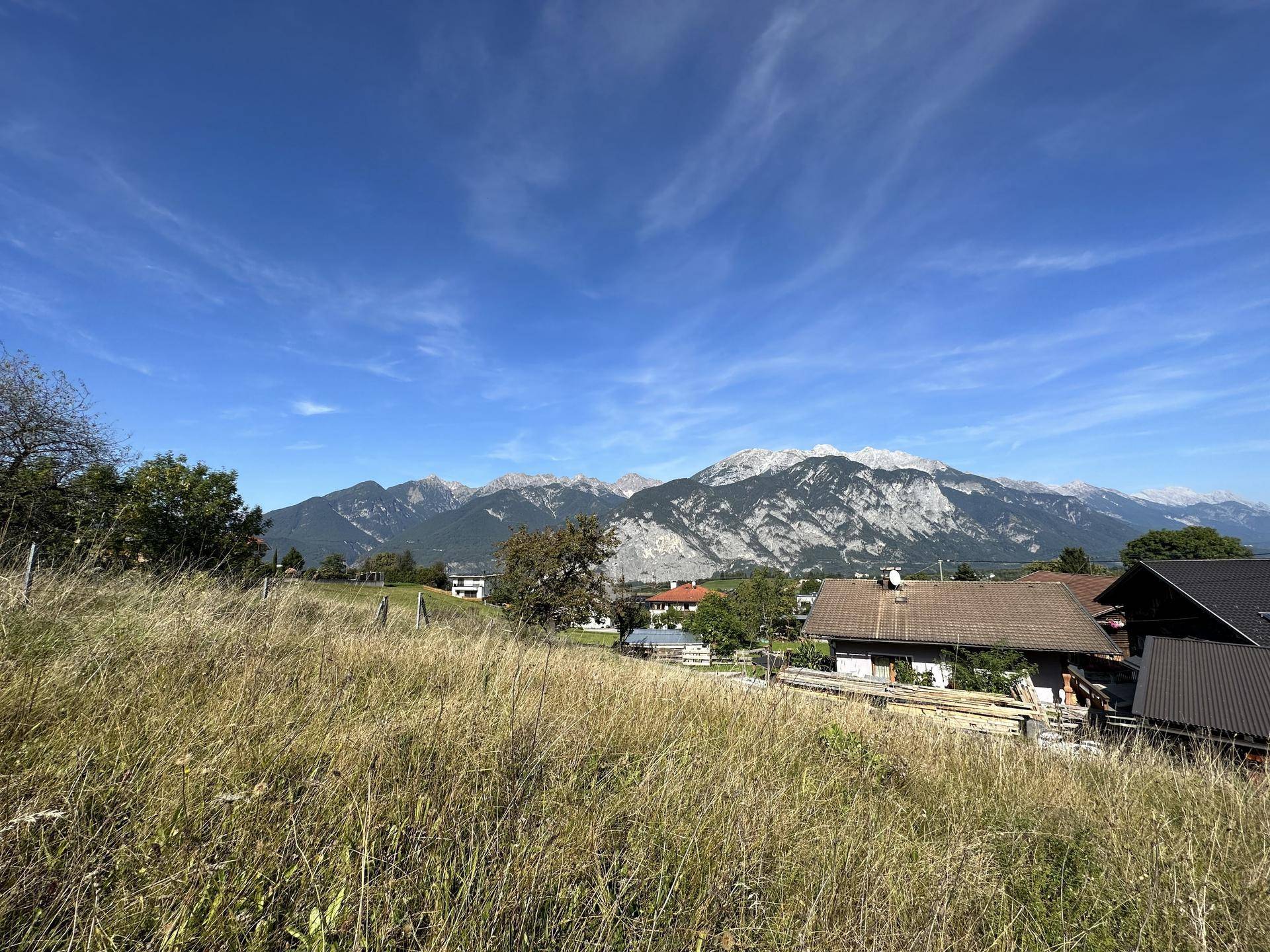 Weitläufiger Blick über eine ländliche Landschaft mit Häusern und majestätischen Bergen im Hintergrund.