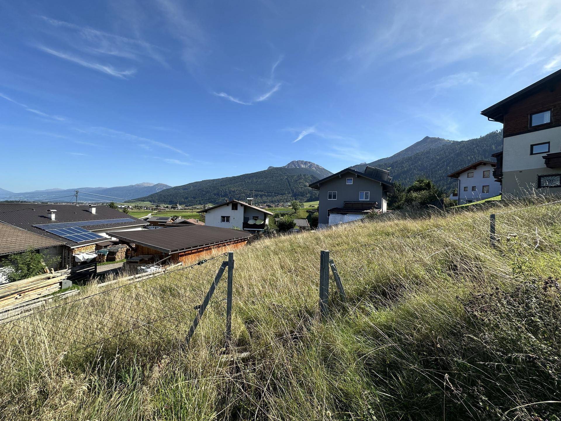 Ländliche Szene mit Wohnhäusern, einem Zaun im Vordergrund und einer weiten Bergkette im Hintergrund.