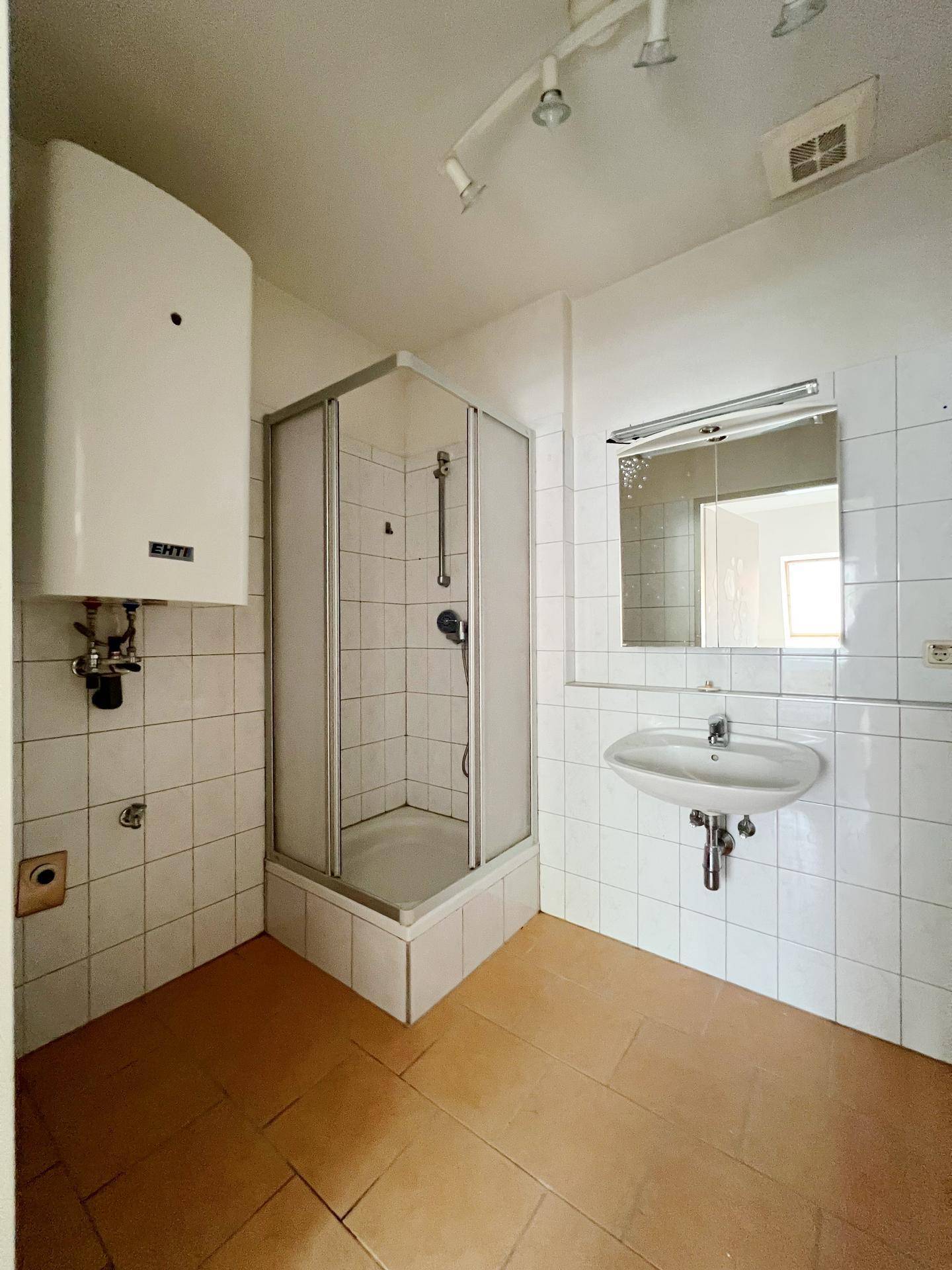 Badezimmer mit Duschkabine, Waschbecken und Boiler, gefliesten Wänden und Boden.