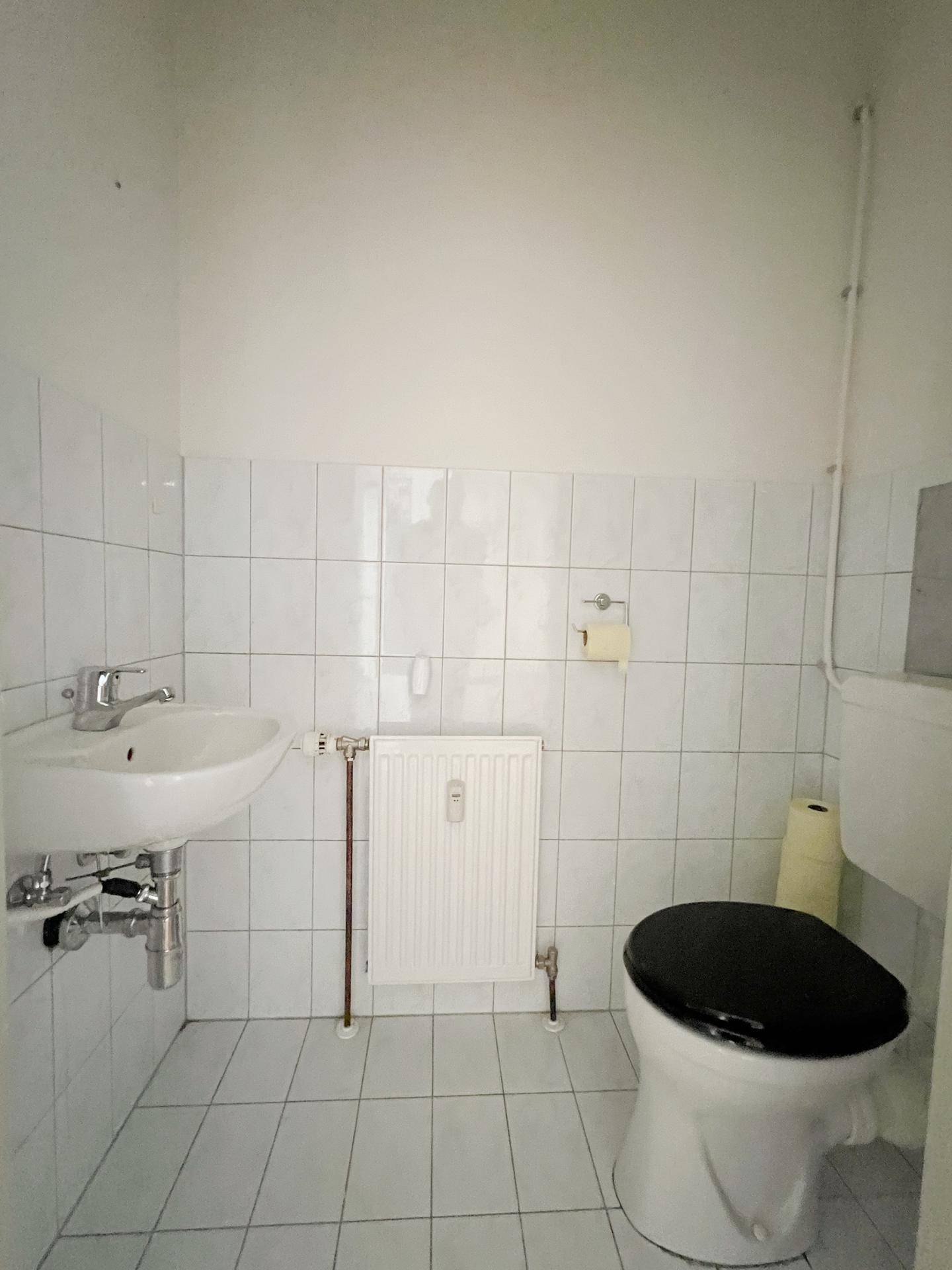 Separates WC mit Toilette, Waschbecken und Heizkörper, komplett gefliest.