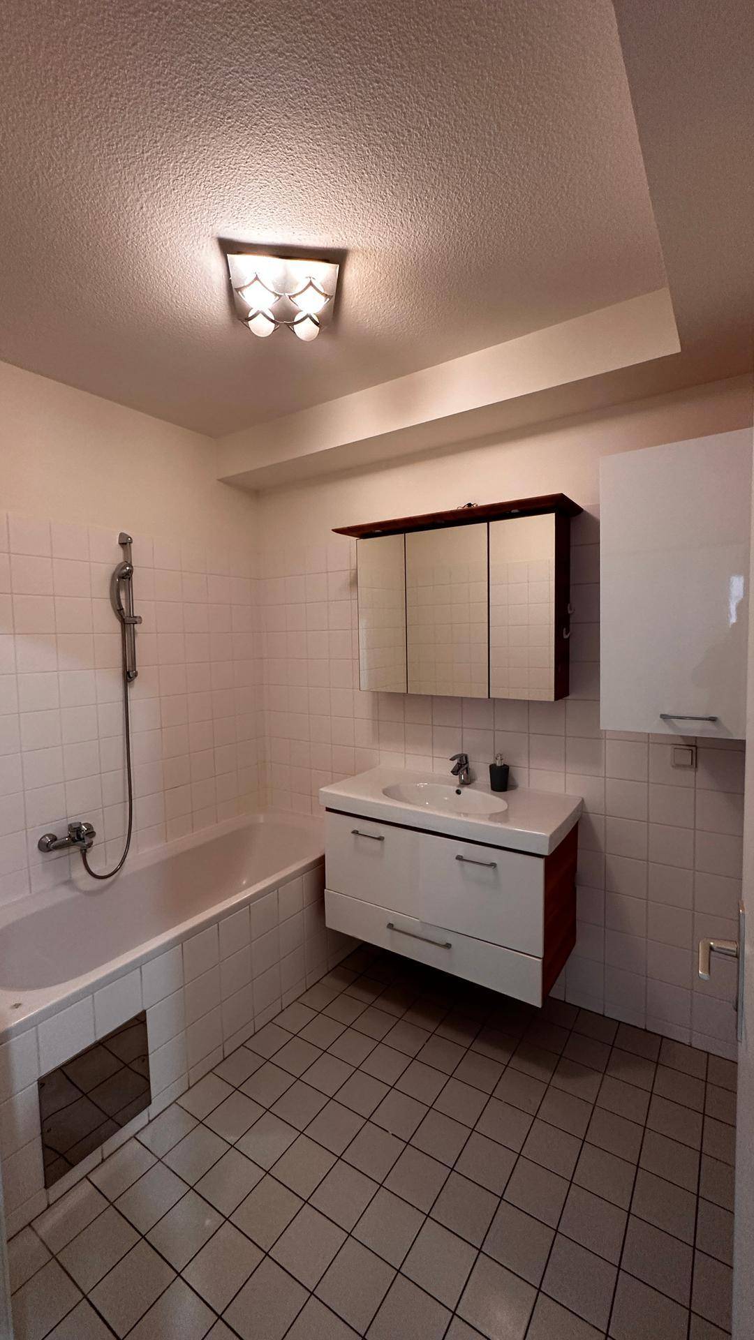 Badezimmer mit Badewanne, Waschtisch und Spiegelschrank, hell gefliest.