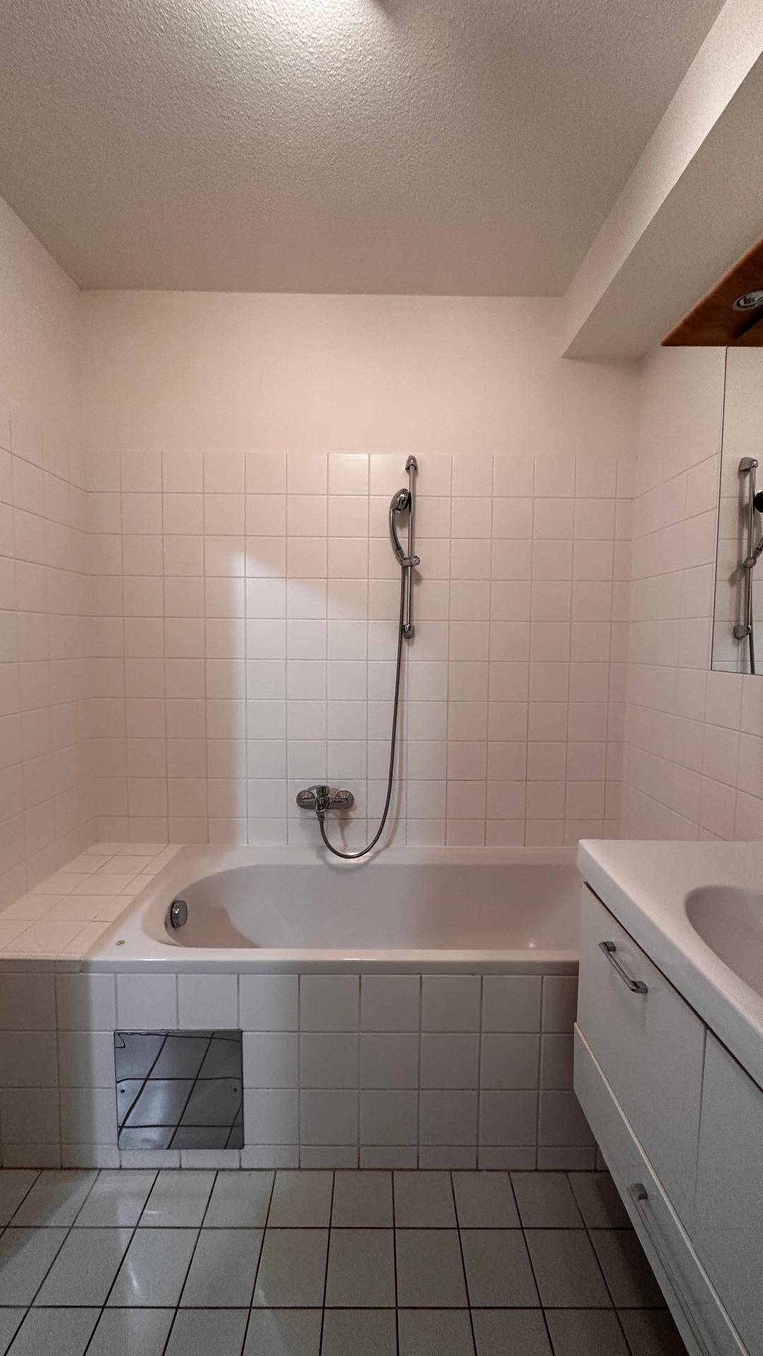 Badezimmer mit Badewanne und Duschfunktion, komplett gefliest in Weiß.