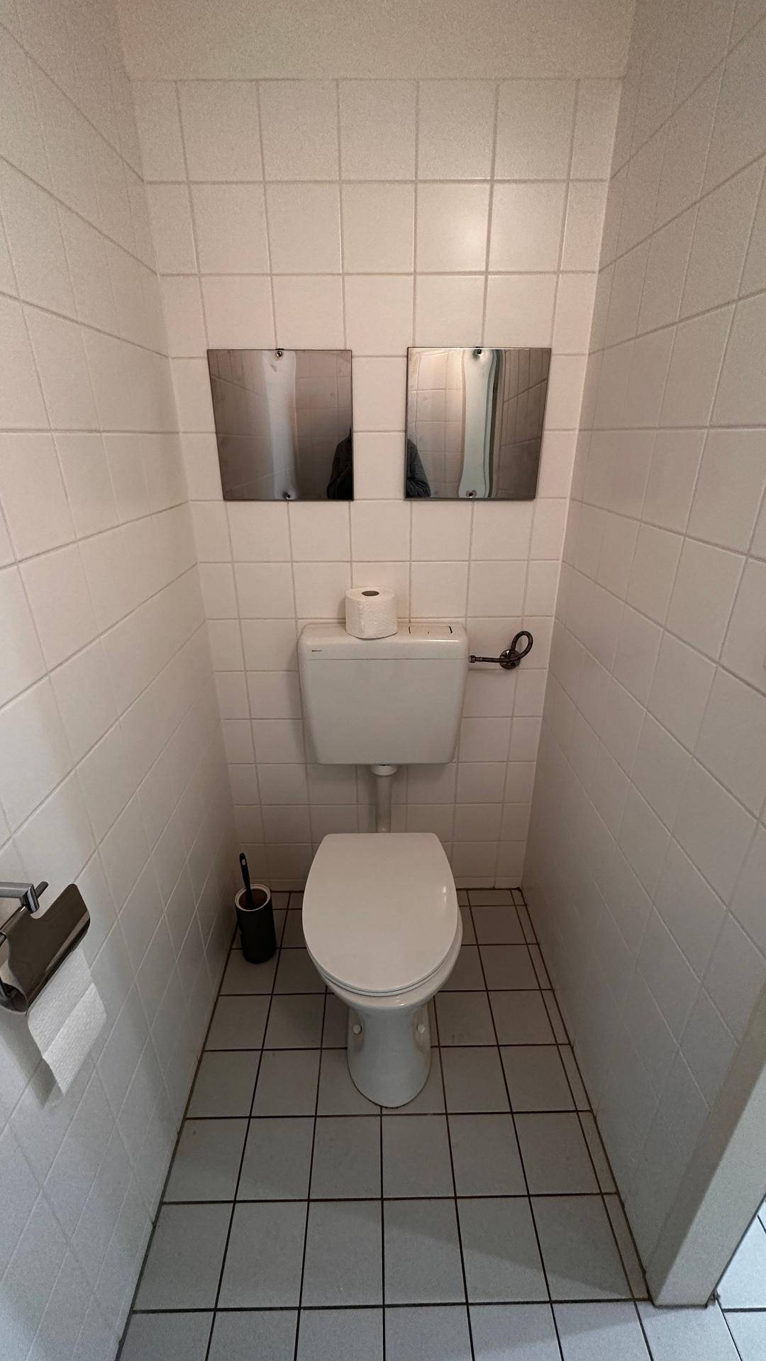 Separates WC mit Toilette und weißen Fliesen an Wänden und Boden.