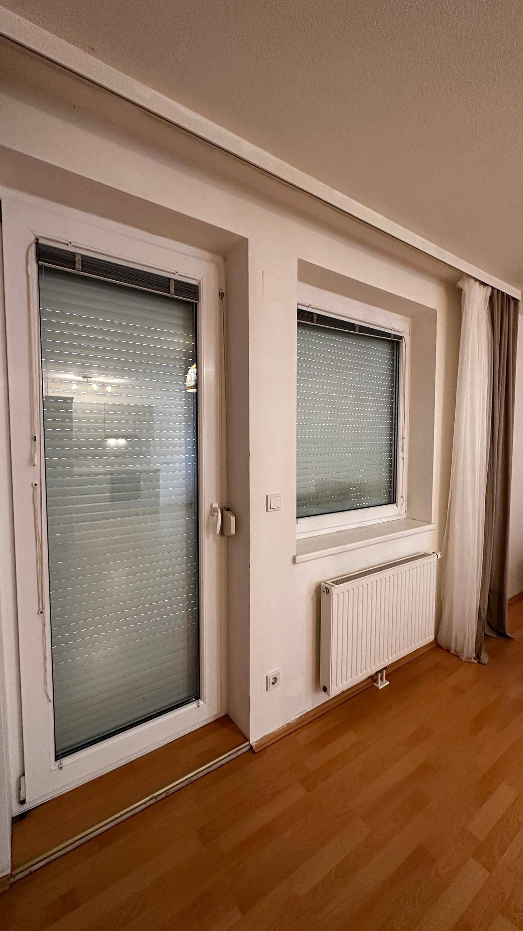 Fenster und Fenstertür mit teilweise geöffneten Jalousien lassen Tageslicht herein.