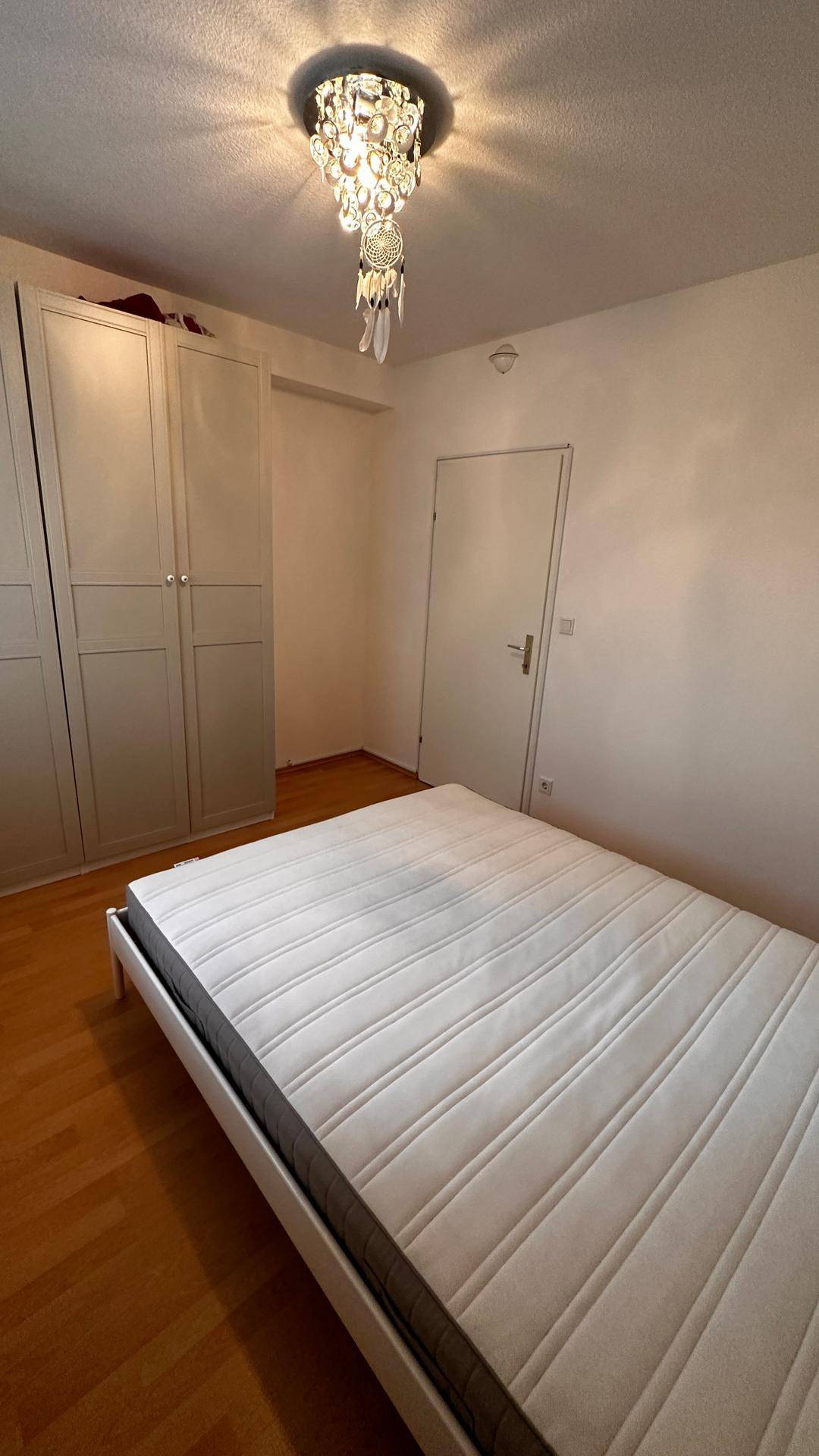 Schlafzimmer mit Doppelbett und Zugangstür, ausgestattet mit Parkettboden.