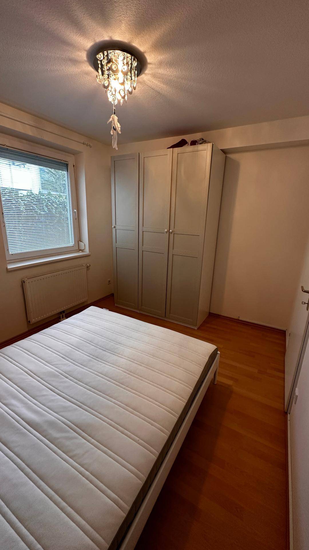 Schlafzimmer mit Doppelbett, großem Kleiderschrank und Fenster mit Jalousien.