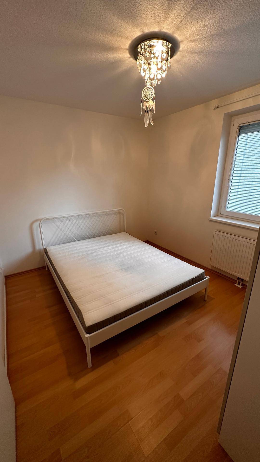 Helles Schlafzimmer mit Doppelbett, Parkettboden und dekorativer Deckenleuchte.