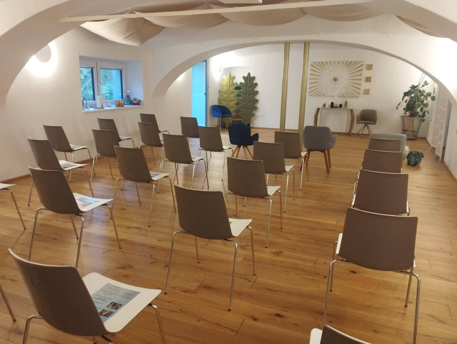 Geräumiger Konferenzraum mit Holzboden, gewölbter Decke und Stühlen, die für eine Veranstaltung bereitstehen.