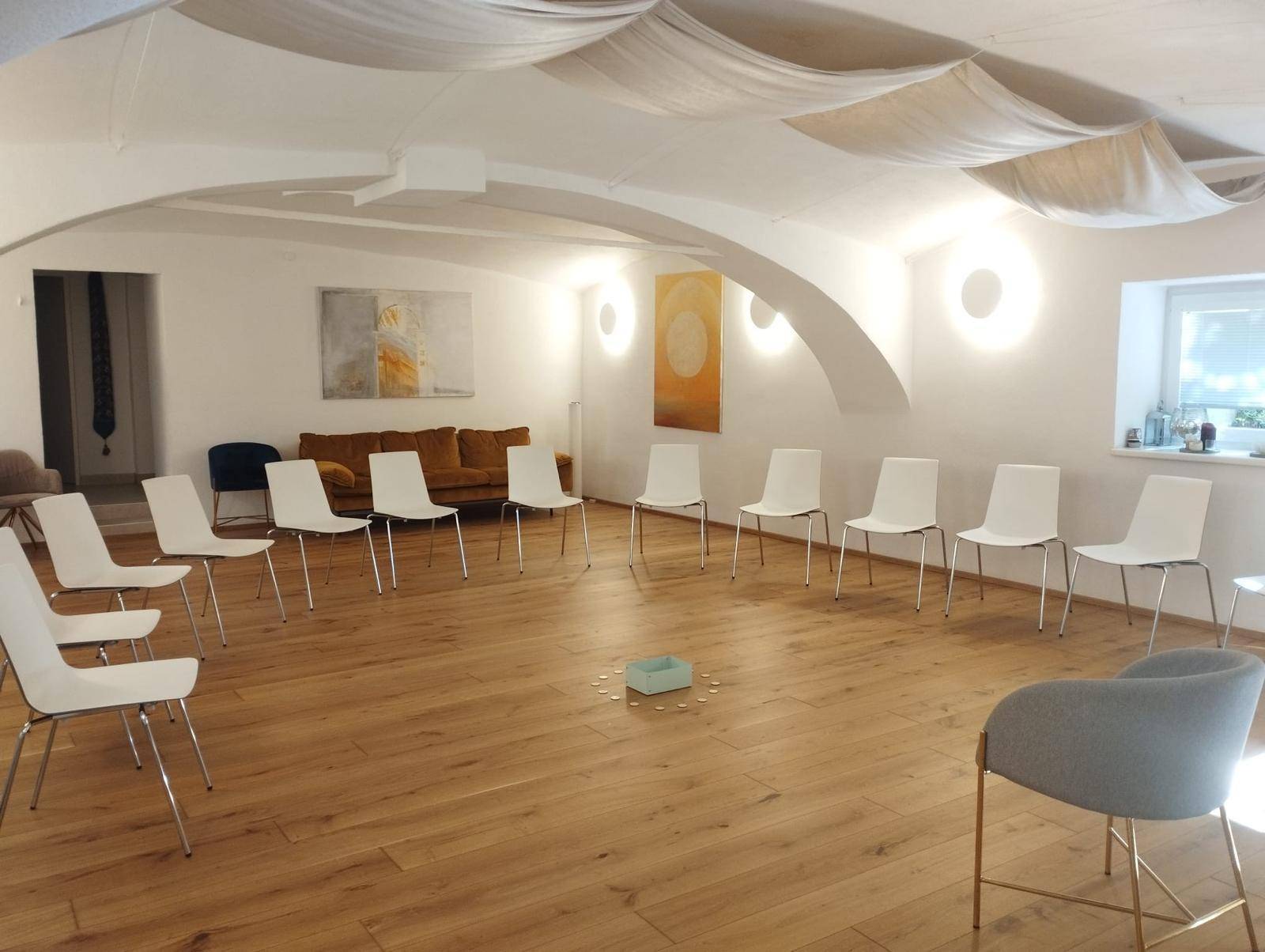 Heller Mehrzweckraum mit Holzboden und Stühlen, die in einem Kreis für Gruppendiskussionen oder Workshops angeordnet sind.