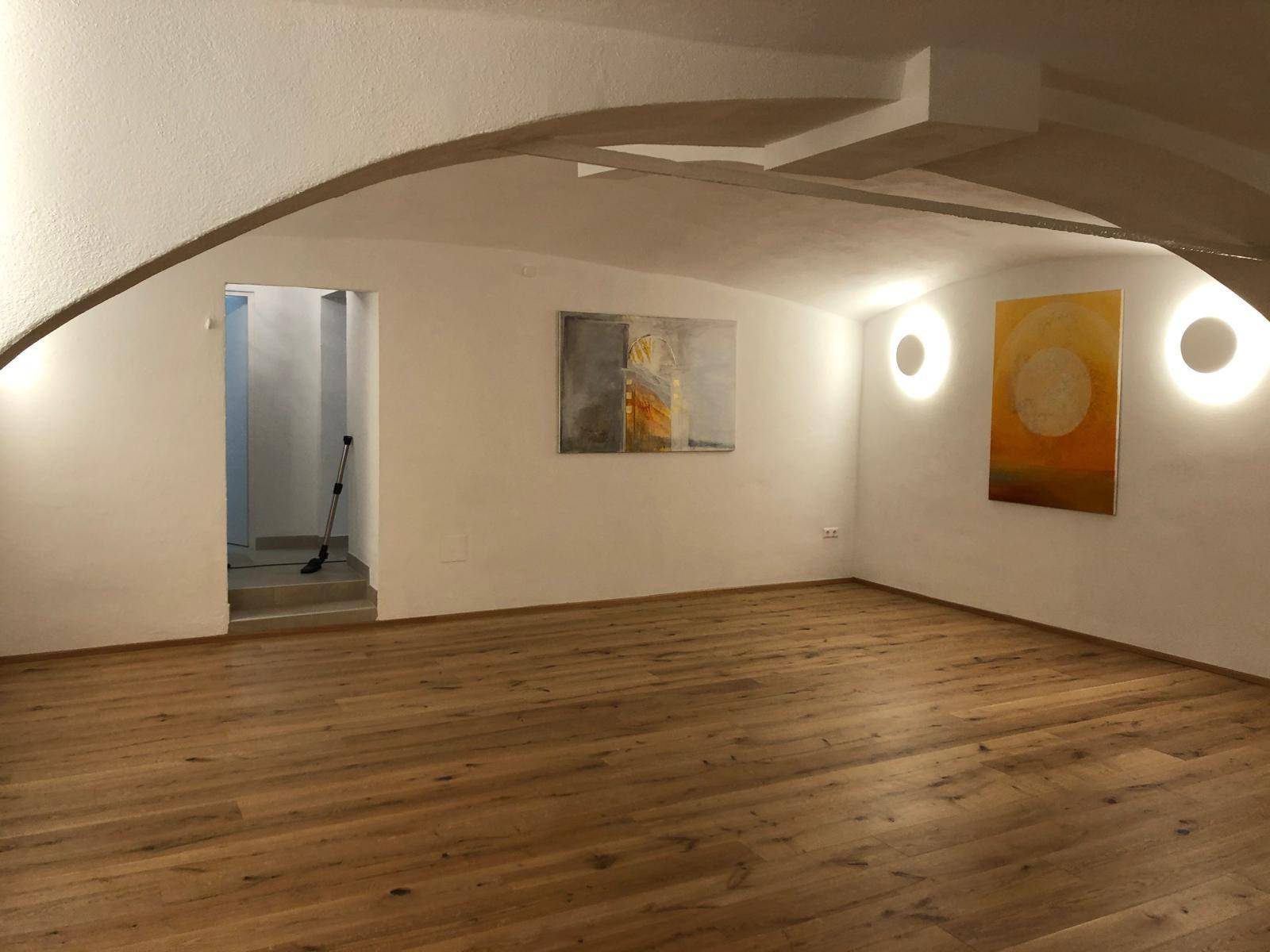 Leerer Mehrzweckraum mit Holzboden, gewölbter Decke und indirekter Beleuchtung, bereit zur individuellen Gestaltung.