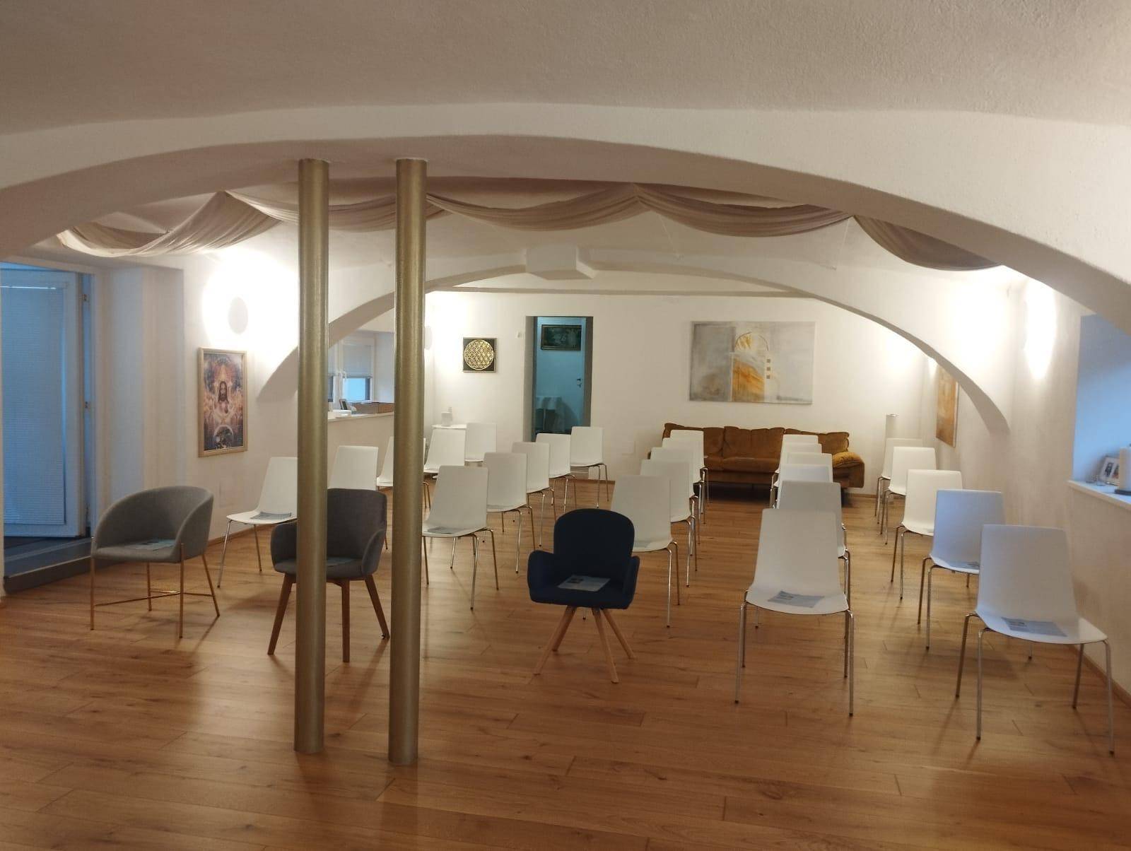 Großer Konferenzraum mit gewölbter Decke, Holzboden und modernen Stühlen, die für eine Veranstaltung aufgestellt sind.