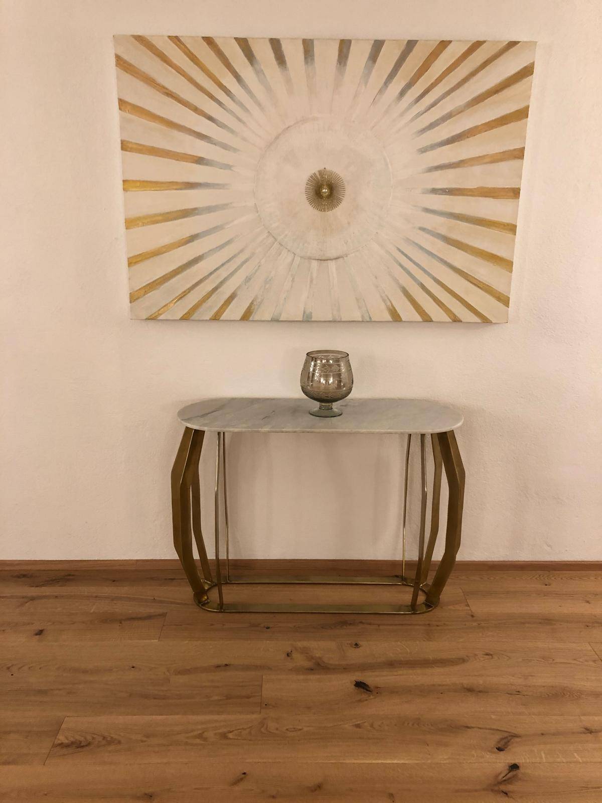 Elegante Konsole mit Marmorplatte und goldfarbenem Gestell unter einem modernen, strahlenförmigen Wandbild.
