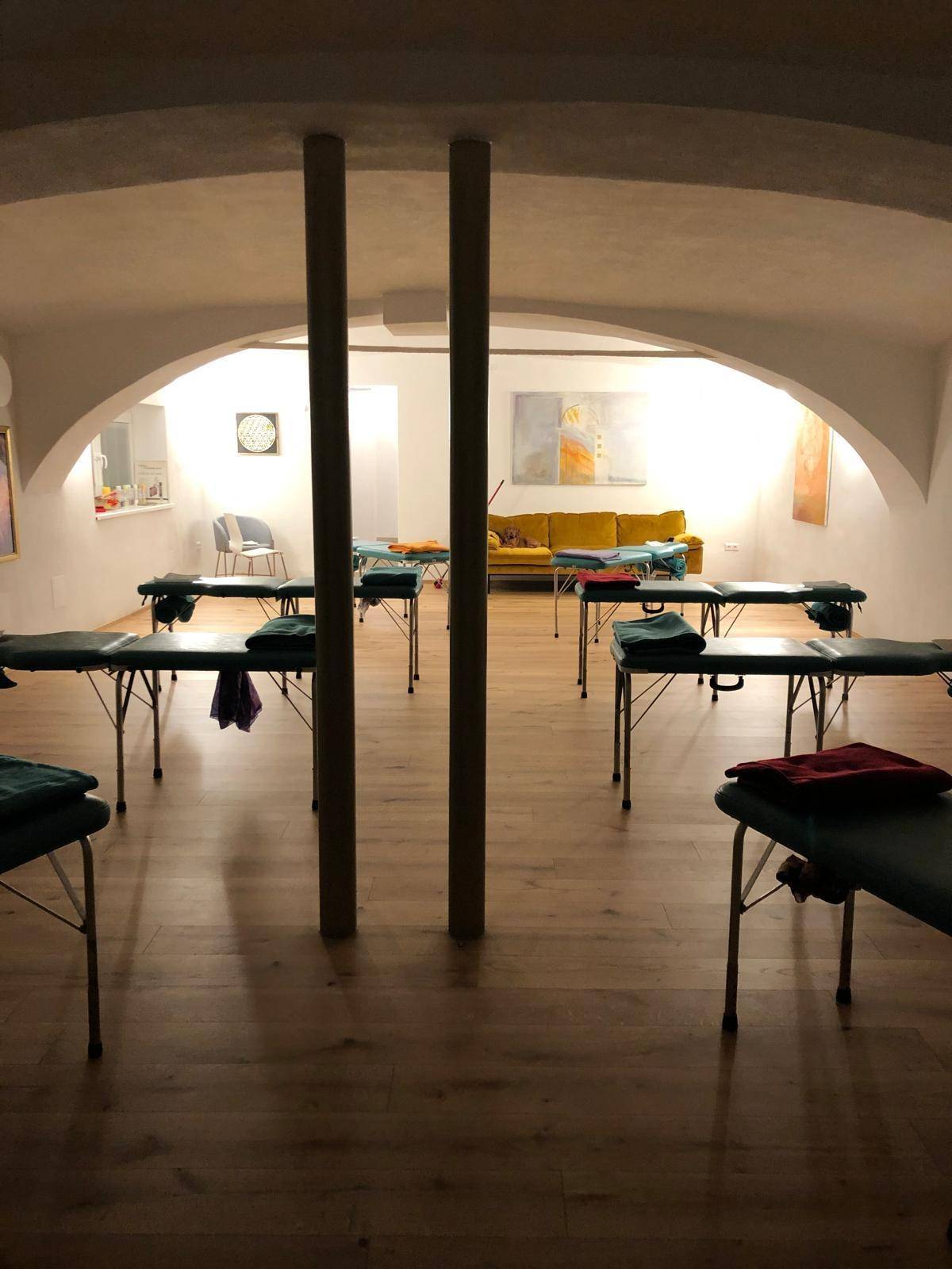 Ruhiger Therapieraum mit Holzboden und mehreren Liegen, ideal für Wellness-Anwendungen oder Behandlungen.