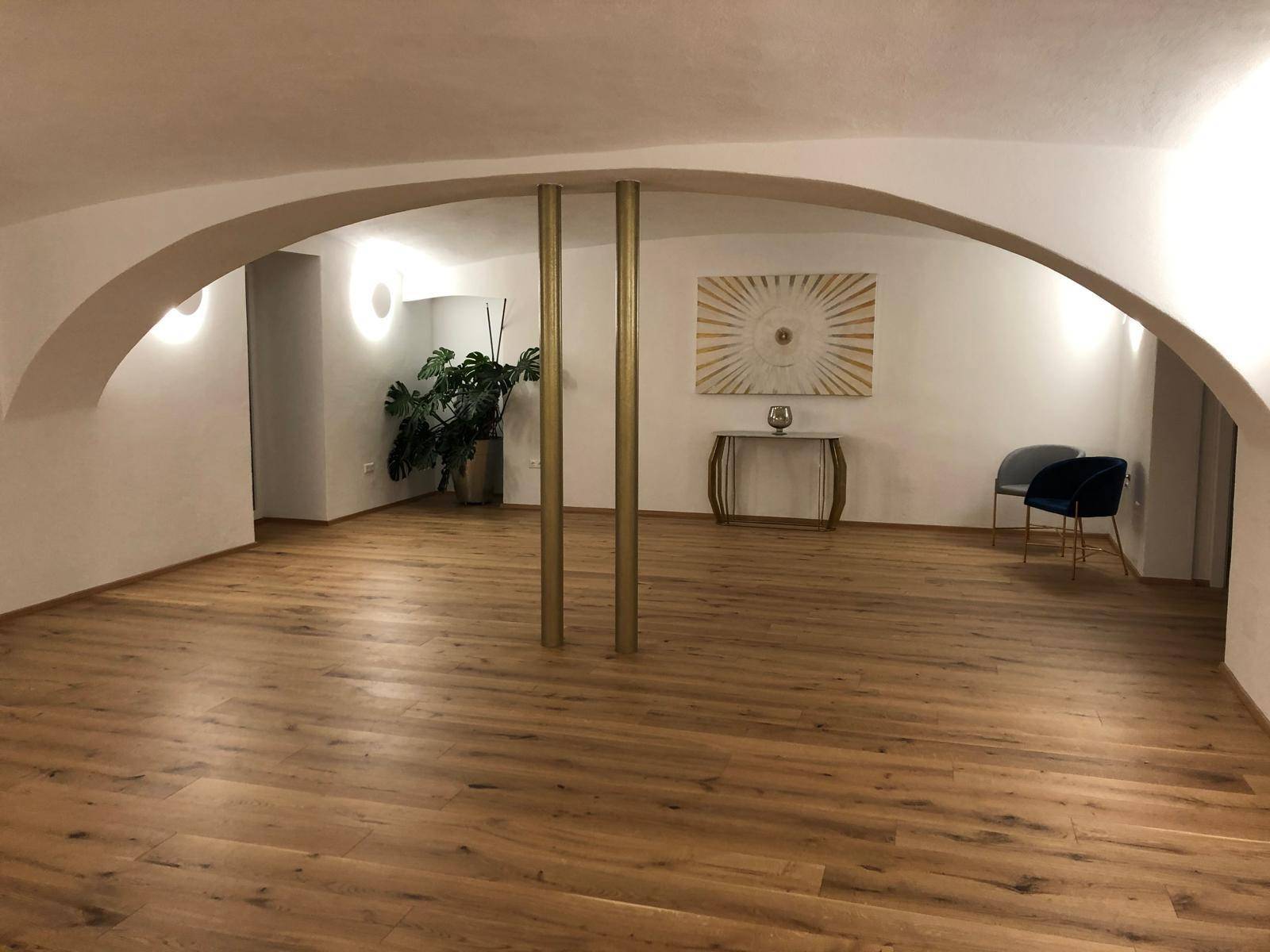 Großer, leerer Raum mit Holzboden, gewölbter Decke und dekorativen Elementen, ideal für verschiedene Nutzungen.