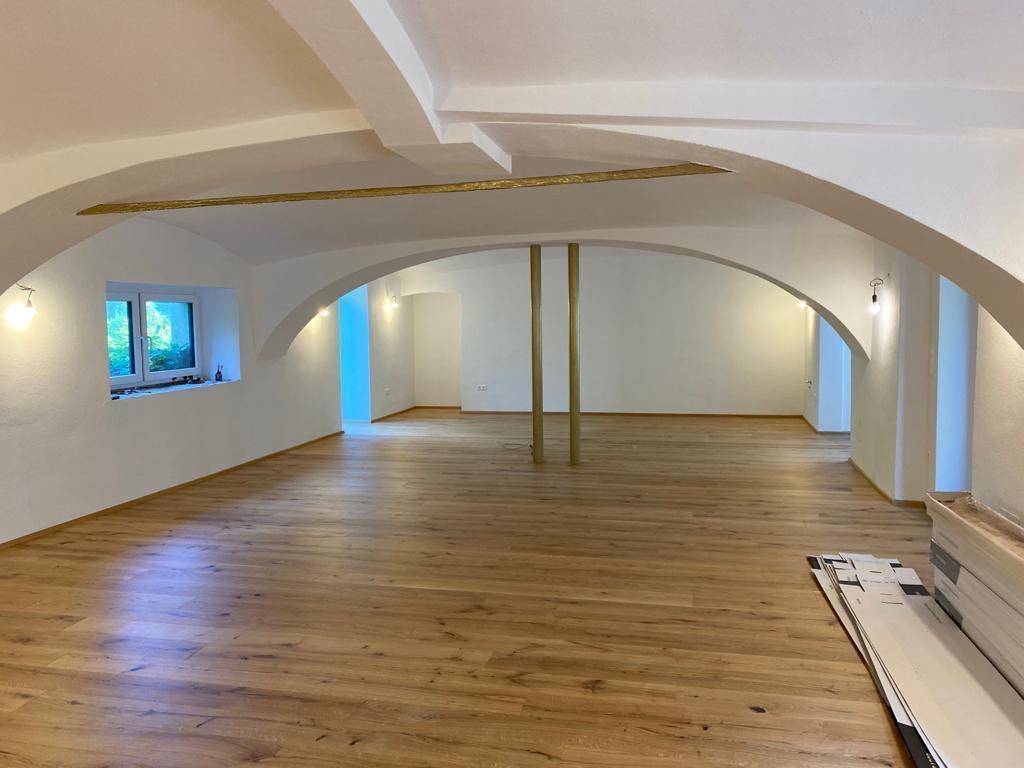 Weitläufiger Raum mit Holzboden, gewölbter Decke und großen Bögen, der vielseitig genutzt werden kann.