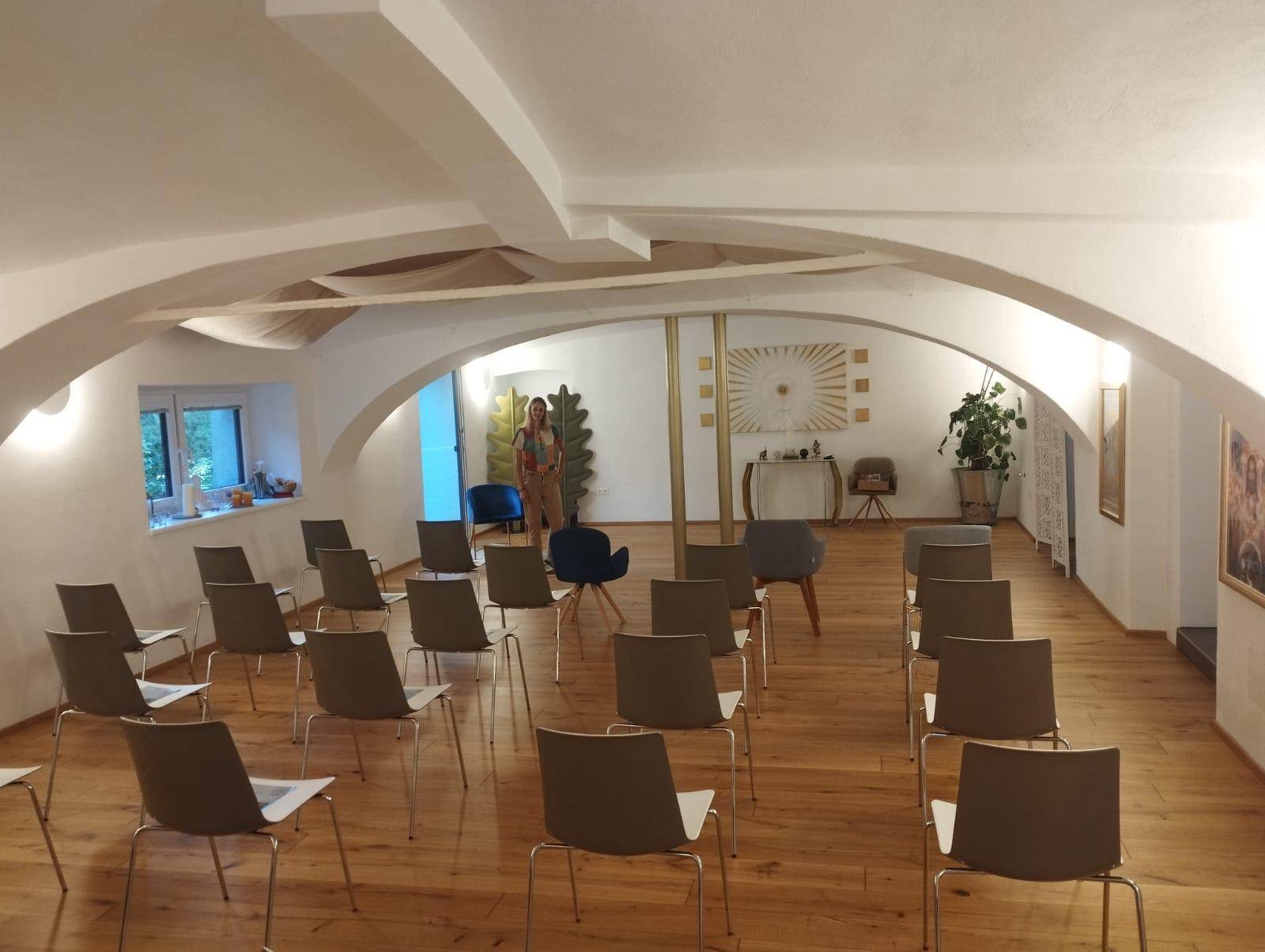 Großer, heller Raum mit Holzboden und Stühlen, die für eine Präsentation oder einen Workshop ausgerichtet sind.