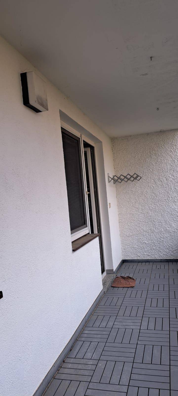 Schmaler Balkon mit grauen Fliesen und weißer Putzfassade, ideal für einen kleinen Außenbereich.