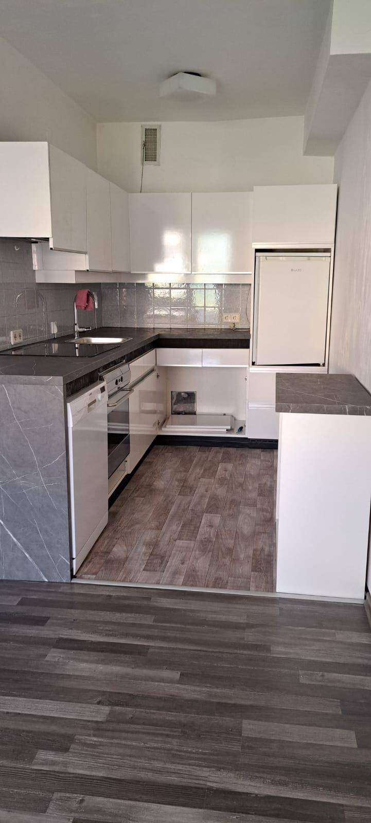 Moderne Küche mit weißen Schränken, dunklen Arbeitsplatten und Holzoptik-Boden.