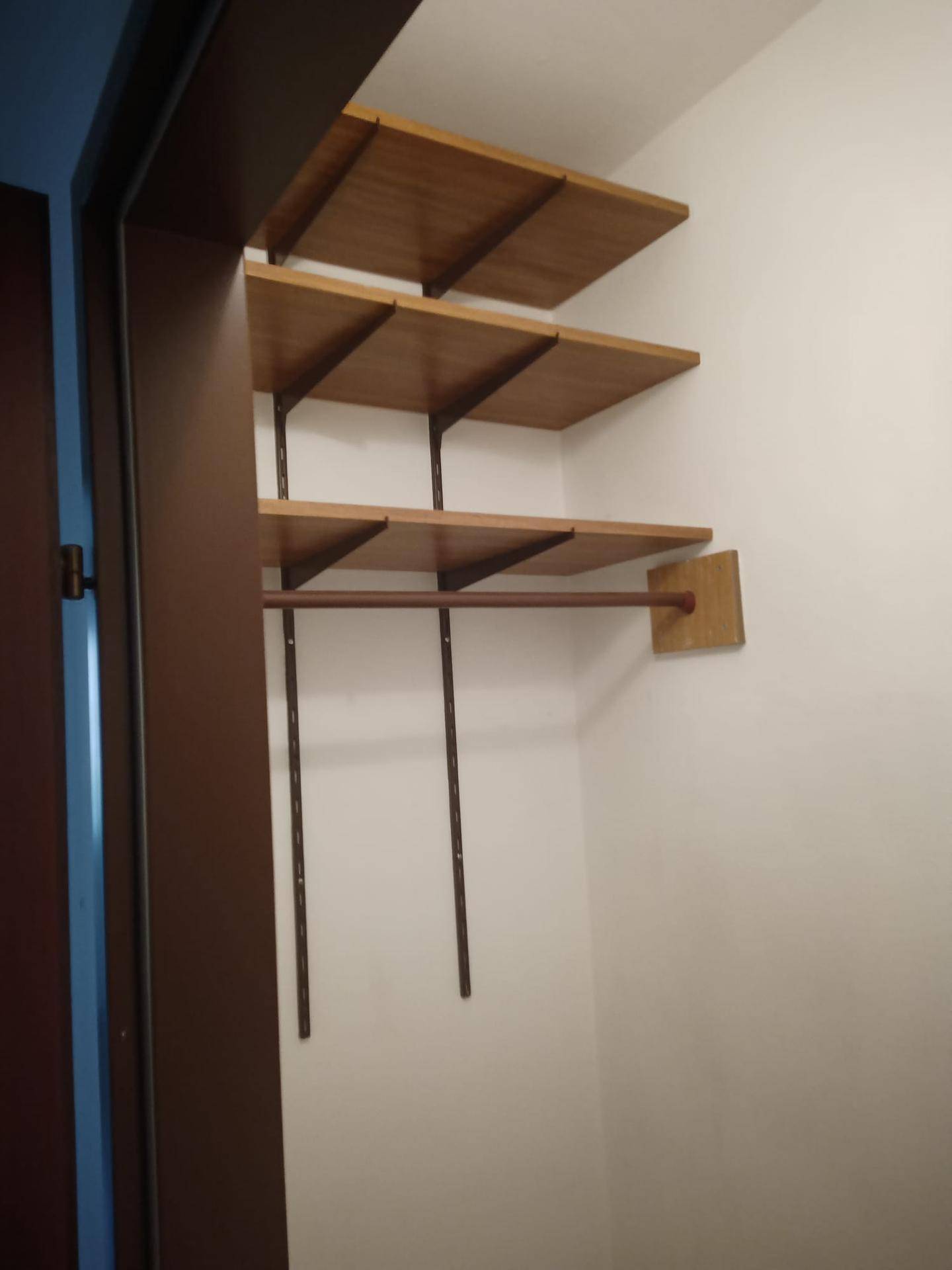 Einfacher Einbauschrank mit Holzregalen und Kleiderstange für zusätzlichen Stauraum.