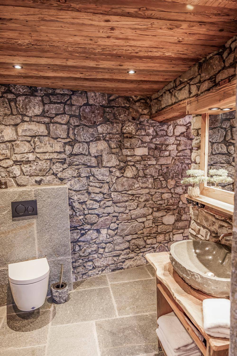 Rustikales Badezimmer mit Natursteinwänden, wandhängender Toilette und Steinwaschbecken.