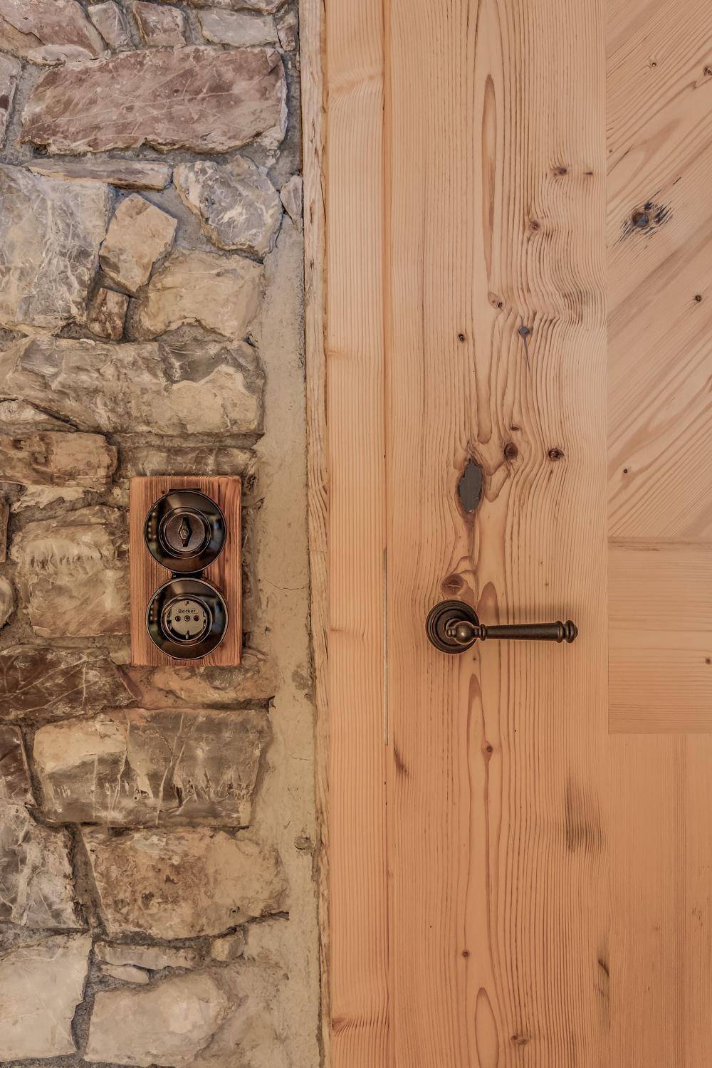Detailaufnahme einer rustikalen Holztür und eines traditionellen Lichtschalters an einer Steinwand.