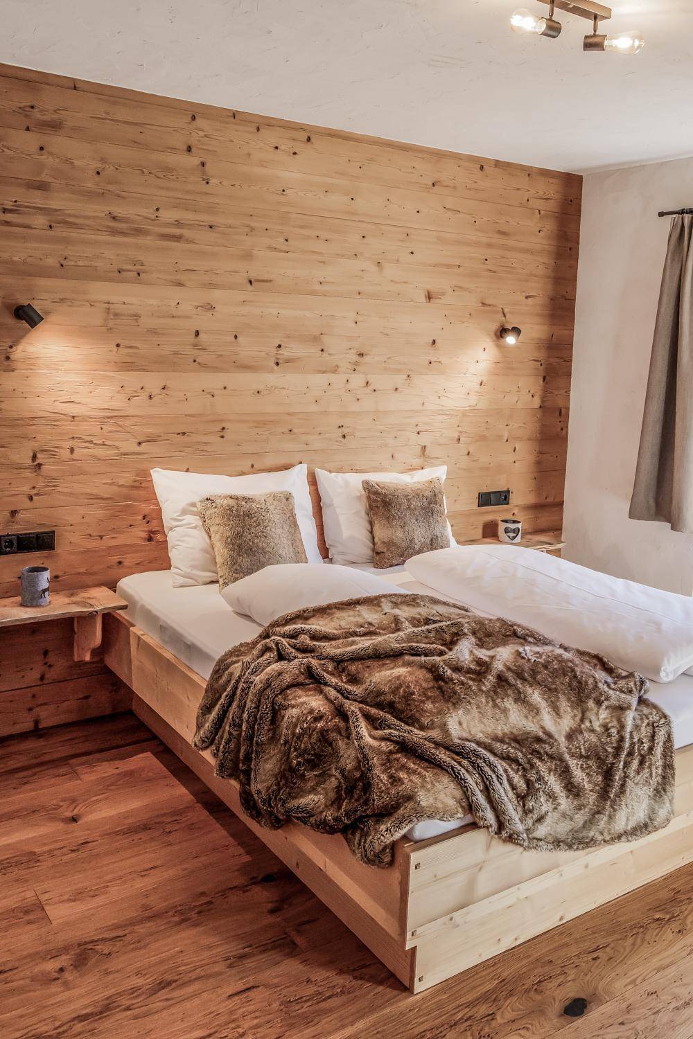 Gemütliches Schlafzimmer mit Holzwandverkleidung, Holzbett und weichen Fellüberwürfen für Komfort.