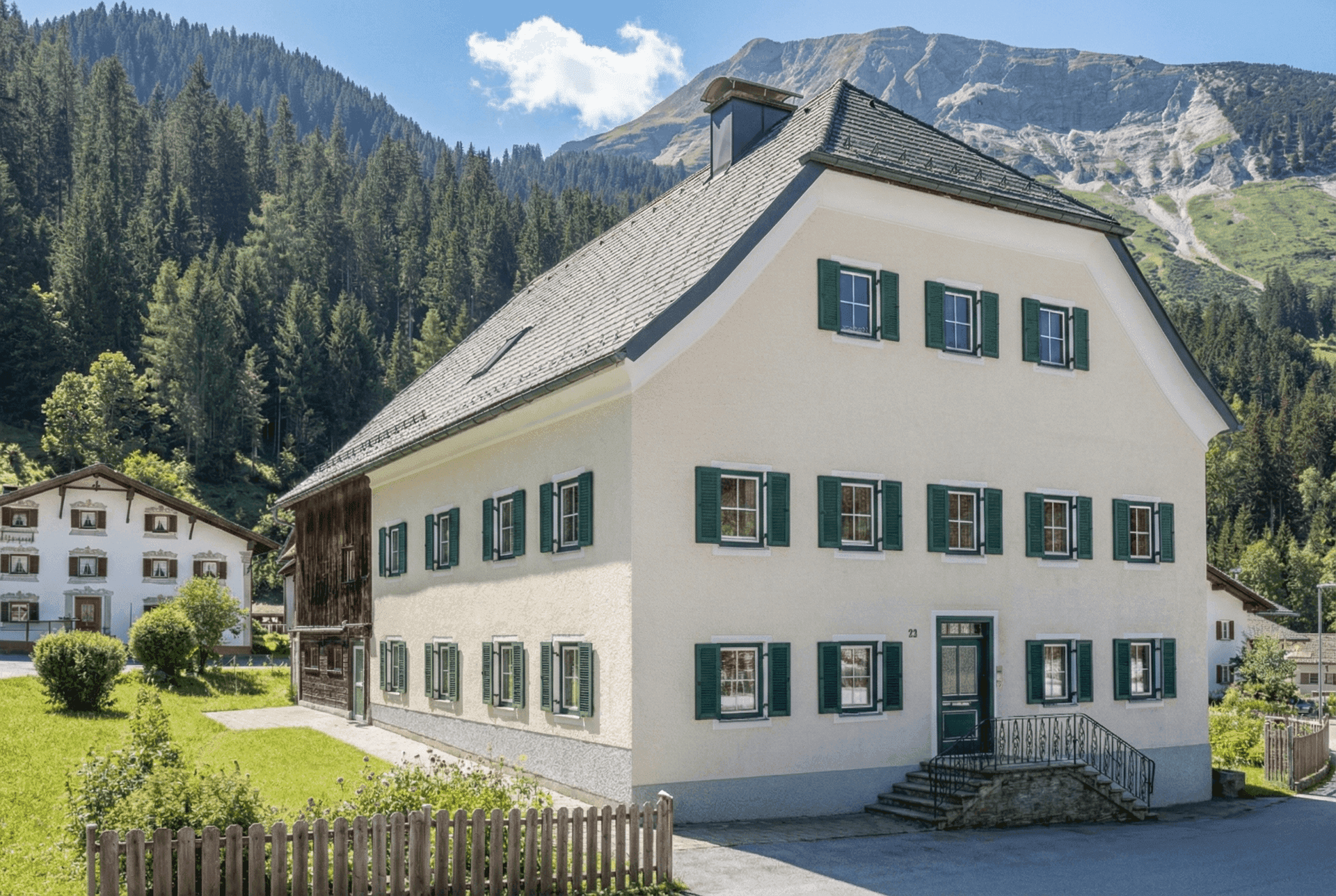 Traditionelles alpines Gebäude mit grünen Fensterläden und Satteldach, eingebettet in eine Berglandschaft.