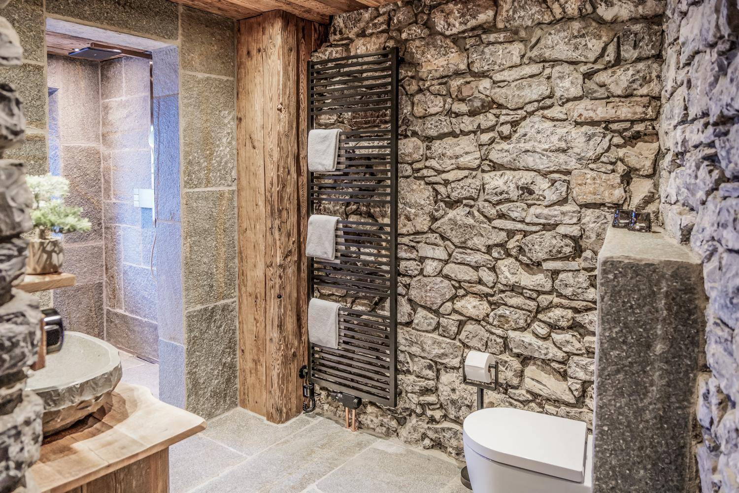 Badezimmer mit Natursteinwänden, beheiztem Handtuchhalter und moderner Toilette.
