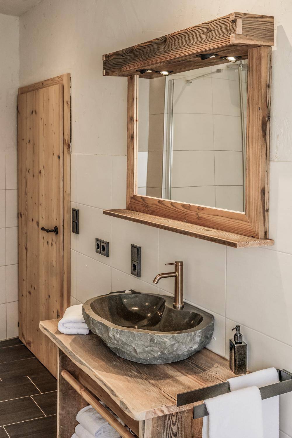 Modernes Badezimmer mit einzigartigem Steinwaschbecken, Holzunterschrank und beleuchtetem Spiegel.