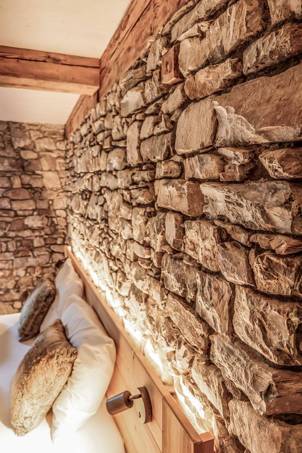 Schlafzimmer mit beeindruckender Natursteinwand und einem Holzbett mit indirekter Beleuchtung.
