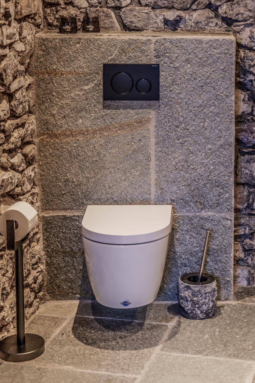 Modernes WC mit wandhängender Toilette und Natursteinwänden sowie passendem Steinboden.
