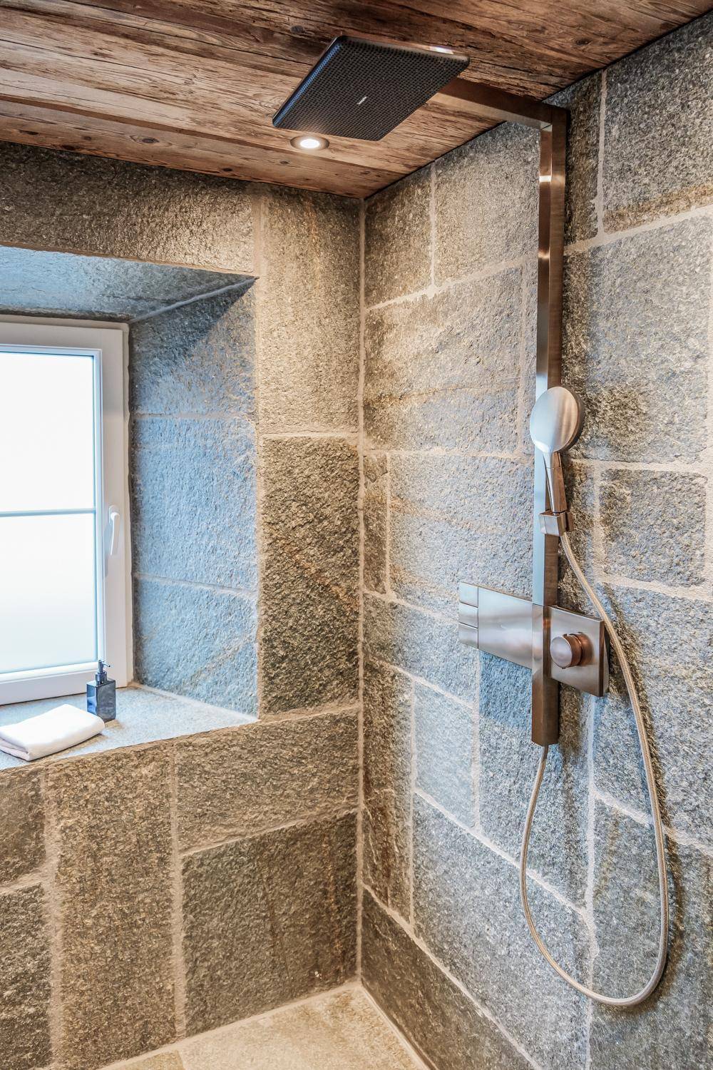 Moderne Dusche mit Natursteinwänden und einer luxuriösen Regendusche.