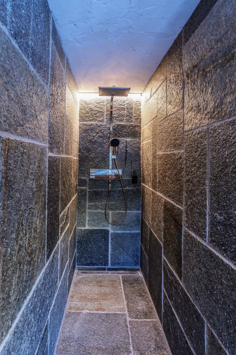 Moderne begehbare Dusche mit dunklen Natursteinfliesen und integrierter Beleuchtung.